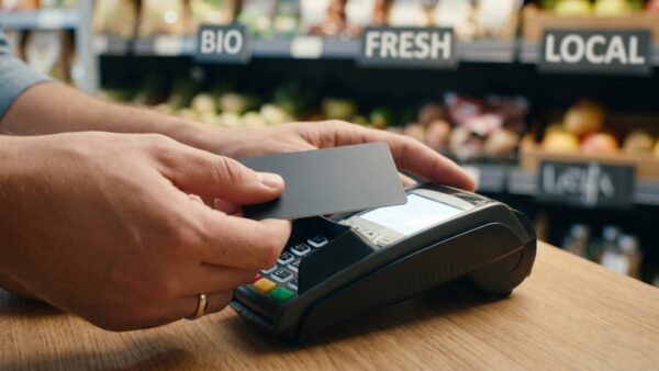 norisbank praemie bild 1 Hände halten eine Bankkarte an ein Kartenterminal an der Ladenkasse