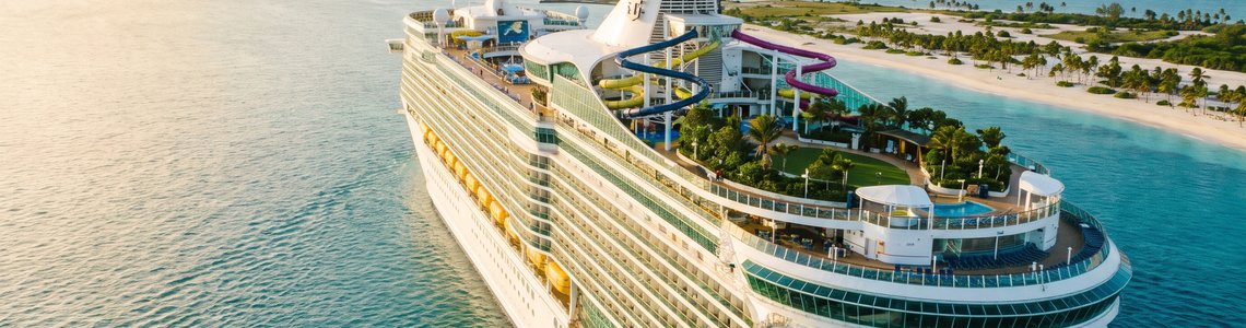 Großes Kreuzfahrtschiff mit vielen Decks vor einer Insel mit Sandstrand und Palmen