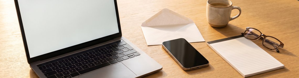 Laptop, Smartphone und geöffneter Briefumschlag auf einem Küchentisch