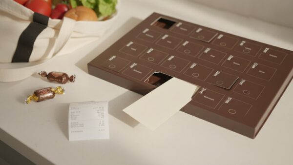 Geöffneter Adventskalender, aus dem ein Papiergutschein ragt, daneben Pralinen und ein Einkaufsbeutel