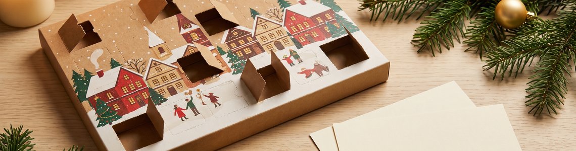 Schokoladen-Adventskalender mit geöffneten Türchen, Tannenzweigen und zwei Papiergutscheinen auf einem Holztisch
