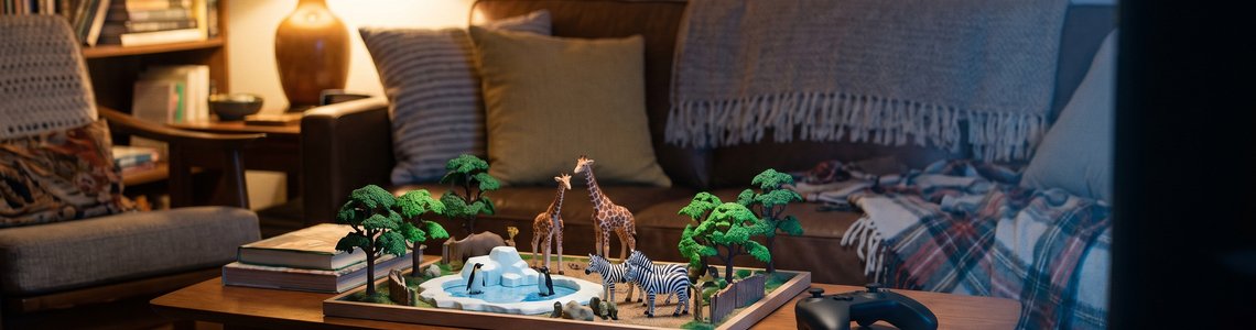 Miniatur-Zoo mit Giraffen, Zebras und Pinguinbecken auf einem Wohnzimmertisch neben einem Gamepad