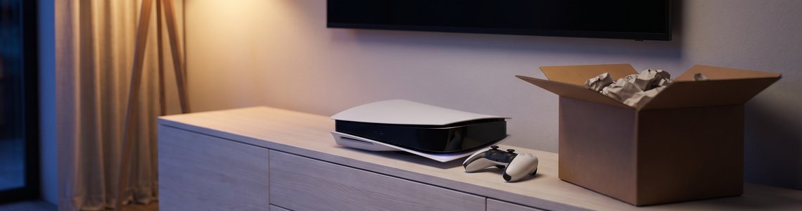 Spielkonsole mit Controller und geöffnetem Versandkarton auf einem TV-Board im Wohnzimmer