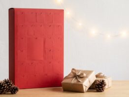 Roter Adventskalender mit geschlossenen Türchen und Geschenkboxen auf einem Holztisch