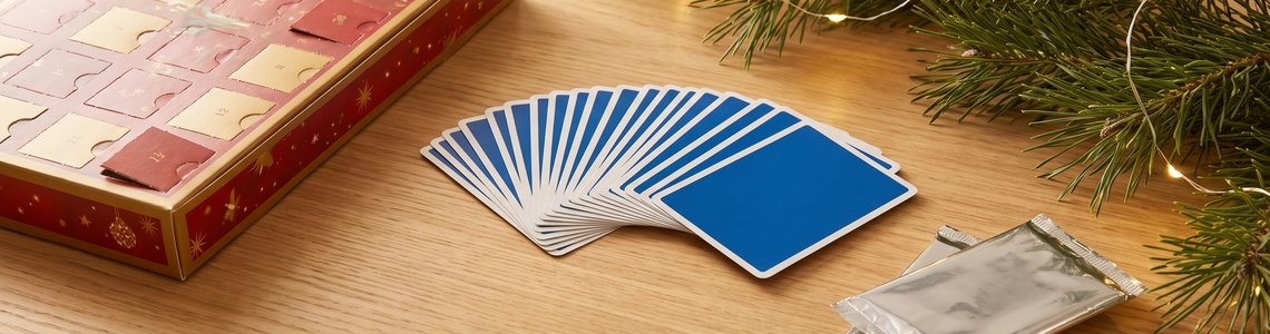 Festlicher Adventskalender neben Sammelkarten, Folienpäckchen und einem Tannenzweig auf einem Holztisch