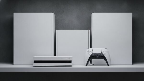 Weiße Spielkonsole und Controller vor drei unbedruckten Kartons auf einer grauen Ablage