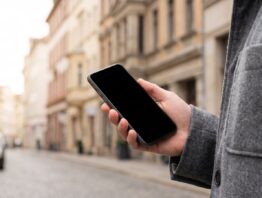 Hand mit Smartphone vor einer unscharfen Innenstadtstraße