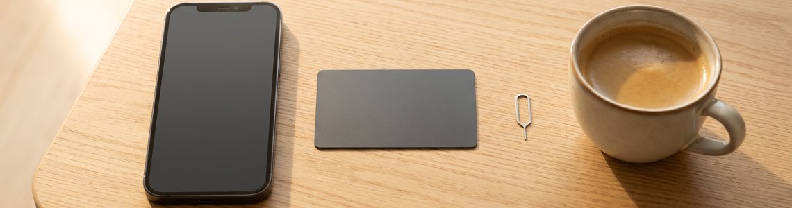 Smartphone, unbedruckte Bezahlkarte und SIM-Werkzeug auf einem hellen Holzschreibtisch
