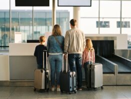 Familie mit Rollkoffern von hinten an einem Check-in-Schalter im Flughafen