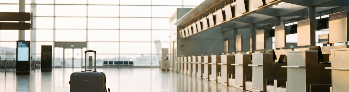Rollkoffer und Rucksack vor leeren Check-in-Schaltern in einem hellen Flughafen-Terminal