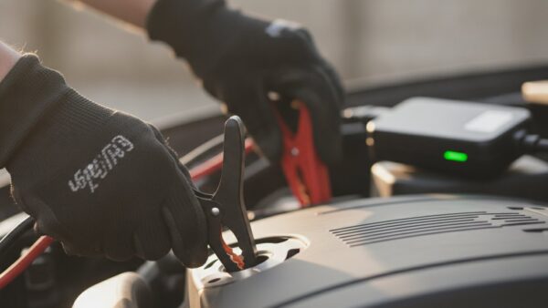 starthilfe powerbank bild 4 Hände in Arbeitshandschuhen setzen die schwarze Polzange an eine Massestelle am Motorblock