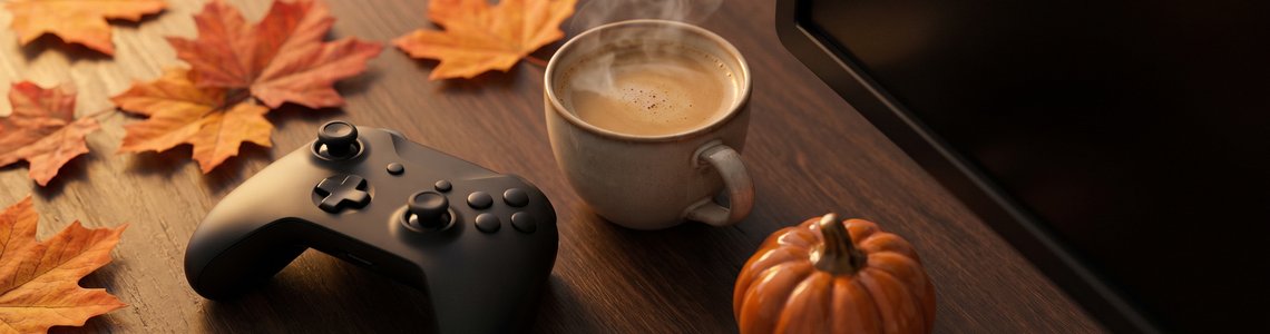 Herbstlicher Schreibtisch mit buntem Laub, einem Gamepad ohne Logo, einer Tasse Milchkaffee und einem Kürbis
