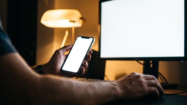 steam login bild 1 Hände halten ein Smartphone vor einen Gaming-Monitor, um die Steam-Anmeldung zu bestätigen