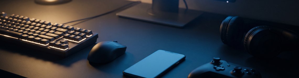 Gaming-Schreibtisch mit Tastatur, Smartphone, Controller und Kopfhörern am Abend