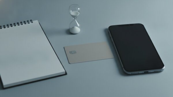 steuervorauszahlung bild 3 Smartphone mit dunklem Bildschirm, neutrale Bankkarte, leerer Notizblock und Sanduhr auf einem Schreibtisch