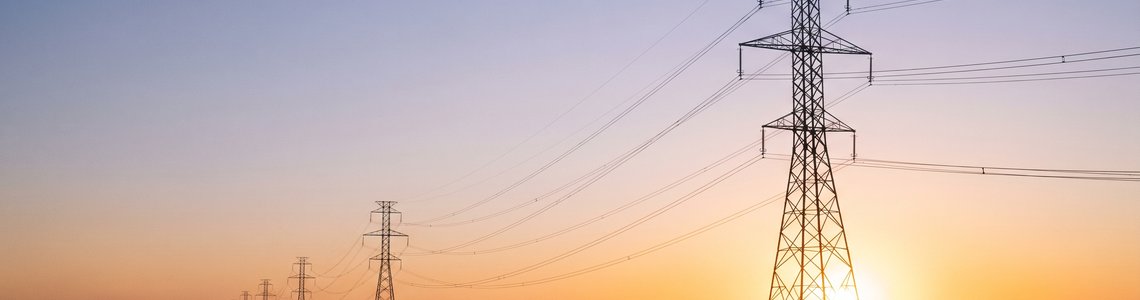 Hochspannungsmasten und Windräder in der Abenddämmerung als Symbolbild für den Strompreis