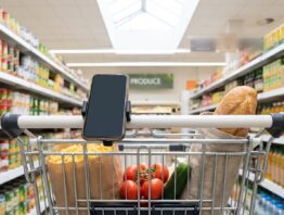 Einkaufswagen mit Lebensmitteln und Smartphone am Griff in einem Supermarktgang