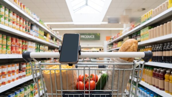 Einkaufswagen mit Lebensmitteln und Smartphone am Griff in einem Supermarktgang