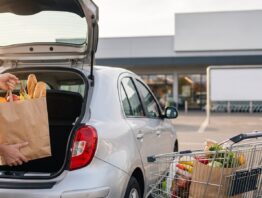 Einkaufswagen am Kofferraum eines Autos auf einem Supermarktparkplatz