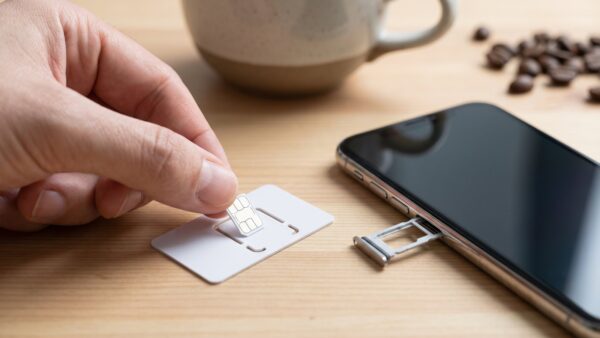tchibo mobil bild 1 Hand löst eine SIM-Karte aus dem Kartenträger neben einem Smartphone auf einem Holztisch