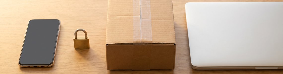 Smartphone, Vorhängeschloss, Versandpaket und Laptop auf einem hellen Holzschreibtisch
