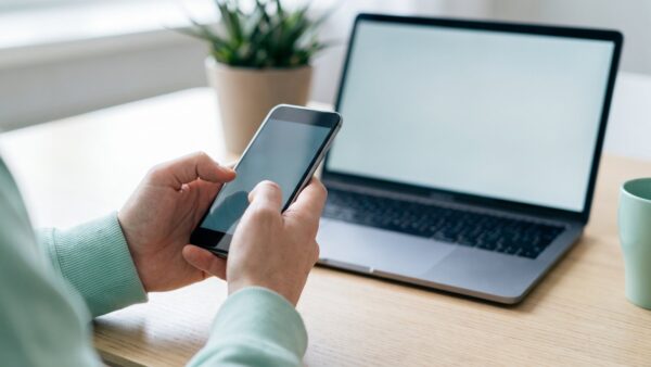 trade republic login bild 1 HĂ€nde halten ein Smartphone vor einem aufgeklappten Laptop bei der Anmeldung im Depot