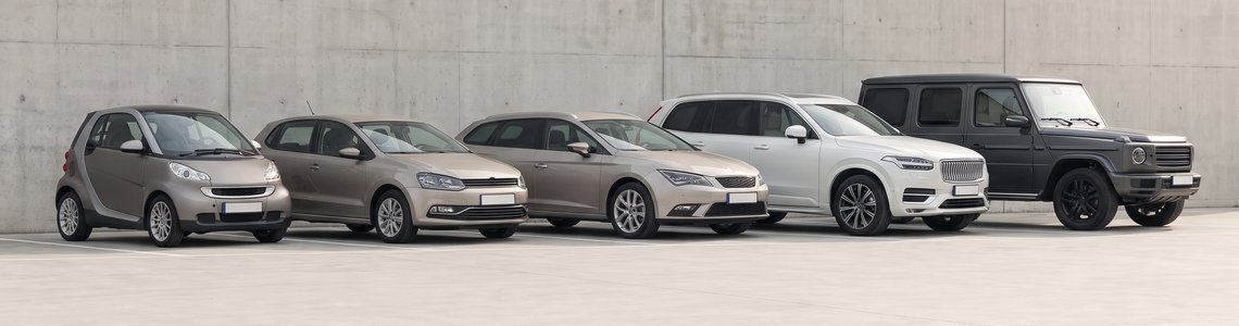 Reihe geparkter Autos vom Kleinwagen bis zum Geländewagen vor einer hellen Betonwand