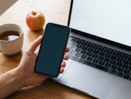 weight watchers login bild 1 Hand mit Smartphone vor einem aufgeklappten Laptop, daneben Tee und ein Apfel, als Sinnbild für den Login in App und Browser