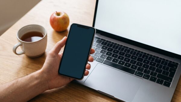 weight watchers login bild 1 Hand mit Smartphone vor einem aufgeklappten Laptop, daneben Tee und ein Apfel, als Sinnbild für den Login in App und Browser