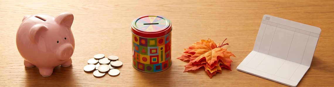 Sparschwein, Münzen, Spardose und Herbstlaub auf einem Holztisch