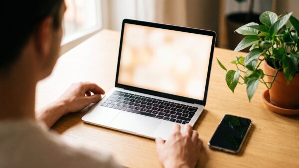 wertgarantie login bild 1 Person von hinten an einem Laptop am Schreibtisch, daneben ein Smartphone â Anmeldung im Wertgarantie Kundenportal