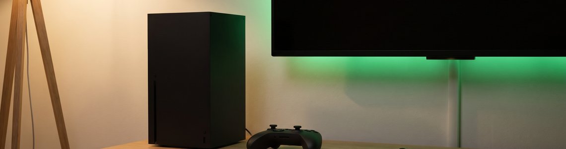 Schwarze Spielkonsole und Controller auf einem Lowboard, daneben ein Schlüsselbund mit Schloss-Anhänger als Symbol für den Xbox Login